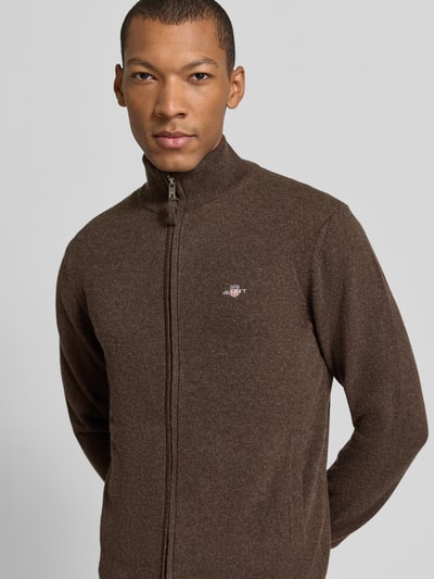 Männermodel trägt Regular Fit Pullover aus reiner Wolle von GANT, jednokolorowy, krój regular fit, wyhaftowane logo, okrągły dekolt, długi rękaw, prążkowane wykończenia, dzianina z wełny, kolor brązowy, Ganzkörperansicht von vorne.