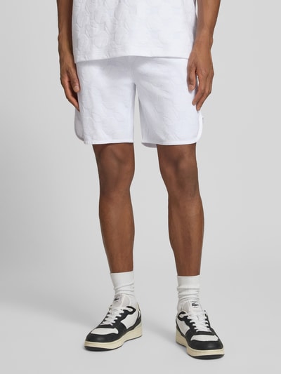 Mężczyzna nosi Regular Fit Shorts aus Baumwoll-Mix Modell 'JT_Member Short' od BOSS Green, białe, gładkie, krój regular fit, grafika strukturalna, elastyczny pas, boczne kieszenie, imitacja kieszeni z tyłu, materiał sweat z bawełnianej mieszanki, zdjęcie całej sylwetki z przodu.