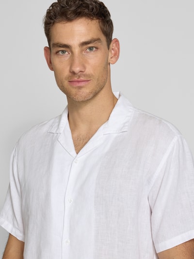 Męski model nosi Regular Fit Leinenhemd mit Reverskragen od MCNEAL, białe, czyste len, krótki rękaw, krój regular fit, zapięcie na guziki, długość tyłu w rozmiarze M: 71 cm, szerokość w rozmiarze M: 50 cm, długość rękawa w rozmiarze M: 30 cm, zbliżenie górnej części ciała.