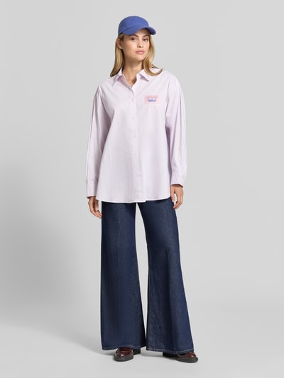 Frauenmodel trägt Oversized Hemdbluse aus Baumwoll-Mix Modell 'SOABIRD' von American Vintage in Hellviolett mit Logo-Patch, Ganzkörperansicht von vorne.