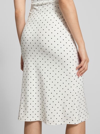Frauenmodel trägt Midirock im Allover-Look Modell '90s' von Gina Tricot in Weiß mit schwarzen Punkten, Material-Mix mit Stretch-Anteil, figurbetonter Schnitt, Nahaufnahme Rückansicht.