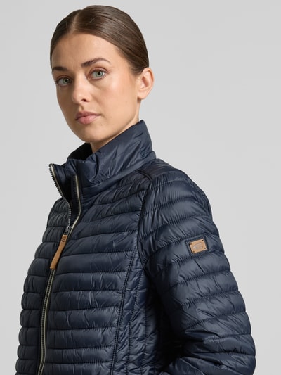 Vrouwenmodel draagt Steppmantel mit Reißverschlusstaschen van camel active in donkerblauw, nauwsluitende pasvorm, detailopname bovenlichaam. Ruglengte maat 36: 75 cm, schouderbreedte 40 cm, borstwijdte 47 cm, mouwlengte 64 cm.