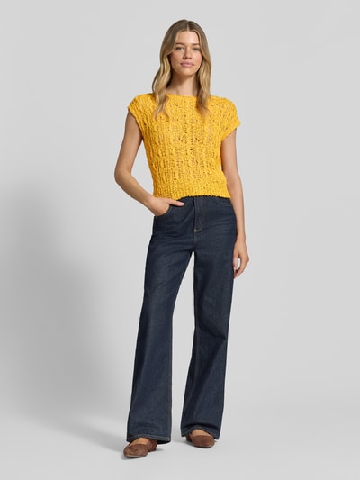 Frauenmodel trägt Strickshirt mit Rundhalsausschnitt von Marc Cain in Gelb, semitransparent, reine Baumwolle, Regular Fit, Kappärmel, kombiniert mit dunkelblauer Jeans, Ganzkörperansicht von vorne.