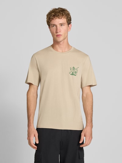 Męski model nosi Regular Fit T-Shirt aus reiner Baumwolle Modell 'BREWY' von JACK & JONES w kolorze beżowym z nadrukiem z napisem, z krótkim rękawem, krój regular fit, bawełna, długość tyłu w rozmiarze M: 68 cm, widok całej sylwetki z przodu.