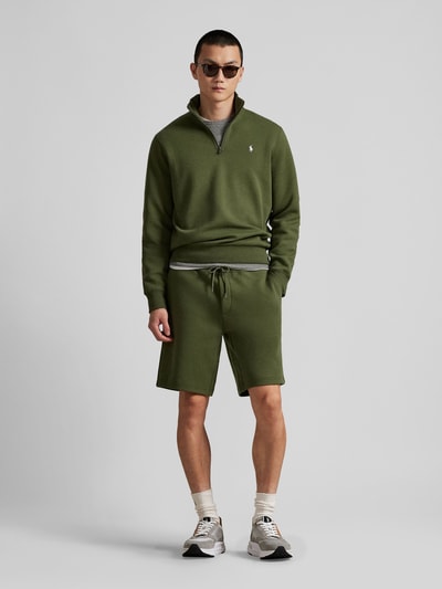 Männermodel trägt Regular Fit Sweatshorts aus Baumwoll-Mix von Polo Ralph Lauren in Olive, unifarben, mit Logo-Stitching, Ganzkörperansicht von vorne.