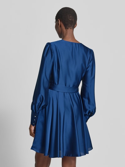 Männermodel trägt Cocktailkleid mit Bindegürtel von Swing, mieszanka materiałów z dodatkiem streczu, taliowany krój, sukienka mini, sukienka kopertowa, dekolt w serek, wiązany pasek, długość tyłu w rozmiarze 36: 87 cm, szerokość w rozmiarze 36: 34 cm, długość rękawów w rozmiarze 36: 70 cm, widok całej sylwetki z tyłu.