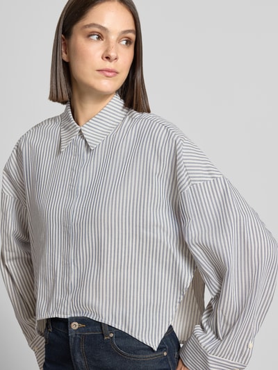 Frauenmodel trägt Relaxed Fit Hemdbluse aus reiner Baumwolle Modell 'OSHIA' von DRYKORN, gestreiftes Design in Hellblau und Weiß, lockere Form mit Hemdblusenkragen und langen Ärmeln, Rückenlänge 57 cm, Ärmellänge 48 cm, Nahaufnahme Oberkörper.