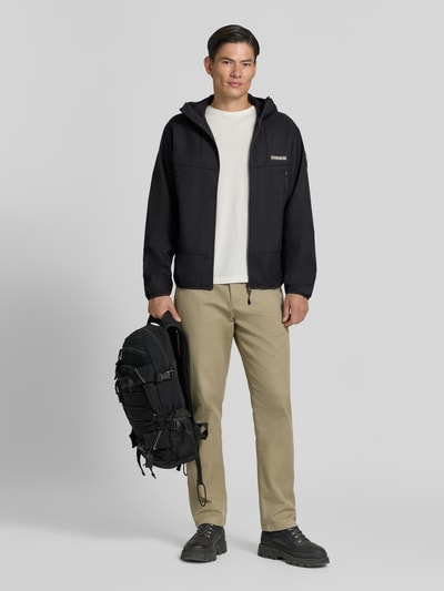 Männermodel trägt Regular Fit Jacke mit Logo-Print von Napapijri in Schwarz, Stehkragen, Eingrifftaschen, Reißverschluss, Ganzkörperansicht von vorne.
