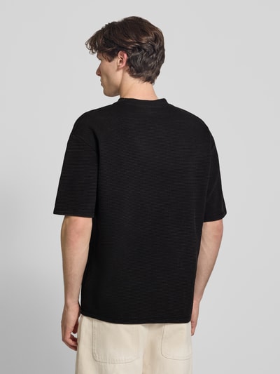 Mannenmodel draagt Oversized T-shirt met structuurpatroon en labelstitching van Pegador, puur katoen, zwarte kleur, ruglengte maat M 70 cm. Ganzekijk rugaanzicht.