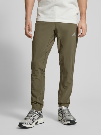 Männermodel trägt Regular Fit Sweatpants mit elastischem Bund mit Logo-Print Modell 'TECH APP S-PANT' von adidas Training, Optik: Unifarben, Passform: Regular-Fit, Label-Print, Logo-Detail, Kontrast-Nähte, Taschen: seitliche Eingrifftaschen, Materialverarbeitung: Batist, Ganzkörperansicht von vorne.