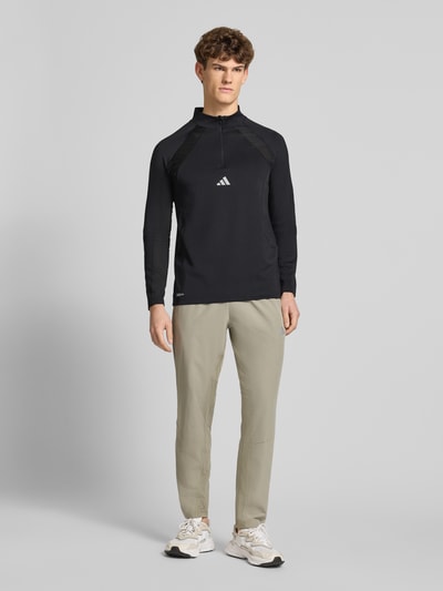Männermodel trägt Sweatshirt mit Stehkragen von adidas Training in Schwarz, Material-Mix mit Stretch, Slim Fit, Label-Print, Ganzkörperansicht von vorne.