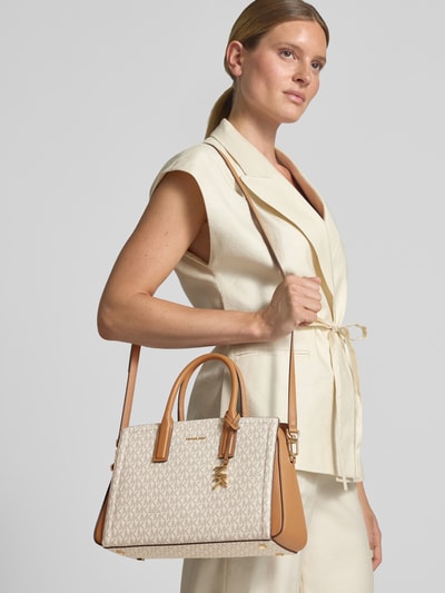 Frauenmodel trägt Handtasche mit Logo-Muster Modell 'LAILA' von MICHAEL Michael Kors in Beige und Braun, Nahaufnahme Oberkörper, Magnetverschluss, Reißverschluss, Label-Applikation, Tragehenkel, Schulterriemen, lederähnliche Textur, Größe 34x22x12 cm, Schulterriemen 130 cm.