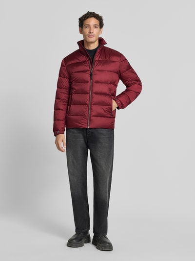 Männermodel trägt Regular Fit Steppjacke mit Stehkragen von JOOP! in Bordeaux, kombiniert mit dunkler Hose, Herren Bomberjacke / Blouson, Ganzkörperansicht von vorne.