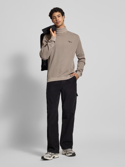Męski model nosi Sweter z golfem w efekt prążkowania z wyhaftowanym logo Rollkragenpullover in Ripp-Optik mit Label-Stitching od Pegador, czysta bawełna, krój relaxed fit, długość tyłu 70 cm, długość rękawów 70 cm, Ganzkörperansicht von vorne.