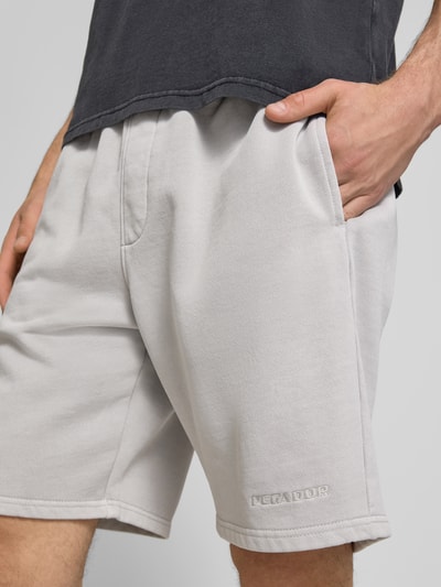 Männermodel trägt Regular Fit Shorts mit Logo-Stitching von Pegador aus Baumwoll-Mix in Hellgrau, Nahaufnahme Oberschenkel.