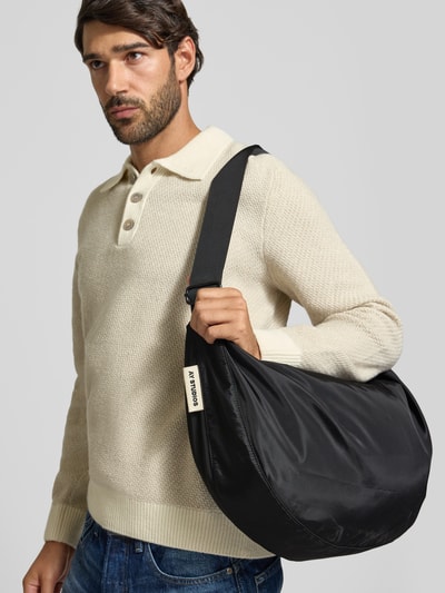 Männermodel trägt schwarze Bauchtasche mit Logo-Detail von AY STUDIOS, Reißverschluss, verstellbarer Schulterriemen, Nahaufnahme Oberkörper.
