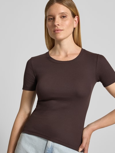 Vrouwenmodel draagt T-shirt met ronde hals model 'ALEXIS' van Samsøe Samsøe in donkerbruin, slim fit, katoen-elastaanmix, ruglengte maat S 54 cm, close-up bovenlichaam vooraanzicht.
