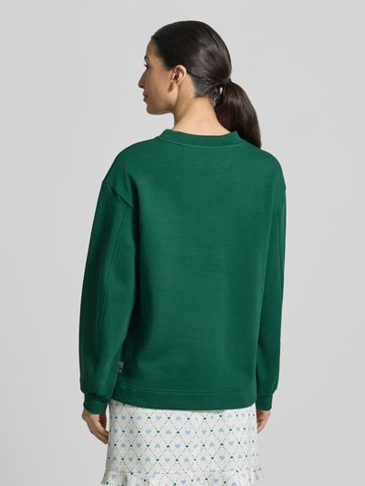 Frauenmodel trägt Relaxed Fit Sweatshirt mit Logo-Detail von Marc Cain in Dunkelgrün, Baumwoll-Mix, elastische Ärmel, Rückansicht Ganzkörperansicht.