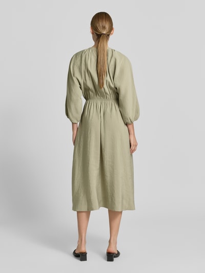 Frauenmodel trägt Midikleid mit Eingrifftaschen Modell 'Worty' von OPUS in hellem Olivgrün, A-Linie, Ganzkörperansicht Rückansicht. Modal-Mix, Schlüsselloch-Ausschnitt, Rückenlänge 121 cm, Brustweite 32 cm, Ärmellänge 35 cm.
