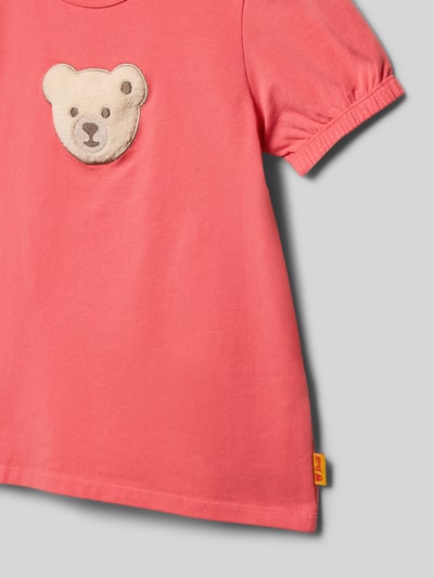 Mädchen trägt Kinder T-Shirt mit Motiv-Stitching und Rundhalsausschnitt von Steiff, Baumwoll-Mix mit Stretch-Anteil, Gerader-Schnitt, Elastische Ärmelabschlüsse, Label-Detail, Farbe Rosa, Rückenlänge 44 cm bei Größe 116, Nahaufnahme Oberkörper.