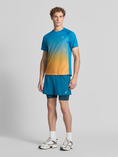 Męski model nosi Regular Fit Shorts mit integrierten Tights Modell 'Road' od ASICS TIGER, niebieski i pomarańczowy, krój regular fit, elastyczny pas, detal z logo, Szerokość w rozmiarze M: 38 cm, Długość wewnętrzna nogawki w rozmiarze M: 12 cm, Ganzkörperansicht von vorne