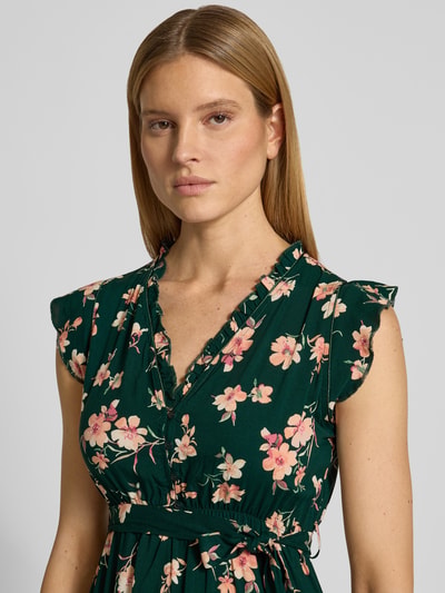 Frauenmodel trägt Kleid aus Viskose mit Bindegürtel und Volantsaum von Apricot, florales Muster, V-Ausschnitt, Nahaufnahme Oberkörper. Taillierter Schnitt, Midikleid, kurze Knopfleiste, Rückenlänge bei Größe S: 94 cm, Brustweite: 51 cm, Ärmellänge: 7 cm.