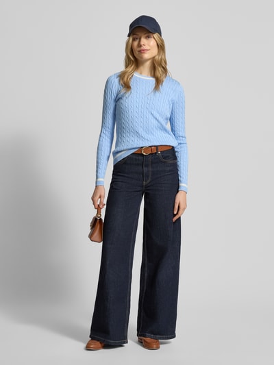Vrouwenmodel draagt Strickpullover mit gerippten Abschlüssen van Christian Berg Woman in lichtblauw, regular fit, katoenmix, ronde hals, textuur met kabelpatroon, gecombineerd met donkerblauwe jeans en bruine accessoires, volledige lichaamsaanzicht van voren.