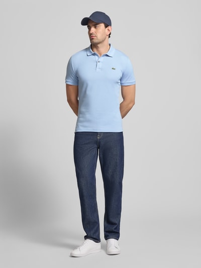 Männermodel trägt Slim Fit Poloshirt aus reiner Baumwolle von Lacoste, Optik: Unifarben, Logo-Stitching, Ganzkörperansicht von vorne.