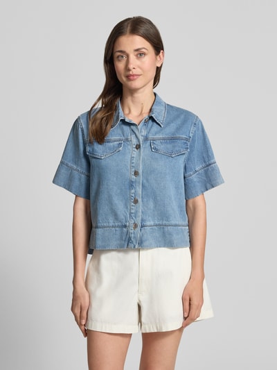 Frauenmodel trägt Boxy Fit Jeansbluse mit Brusttaschen Modell 'LAIKA' von SUNCOO PARIS aus Lyocell-Baumwoll-Mix, Hemdblusenkragen, kurzarm, helle Denim-Optik, mittlere Waschung, sichtbare Nähte, ganz leicht strukturierte Oberfläche, Vorderseite mit Knopfleiste, Rückenlänge bei Größe S: 52 cm, Ärmellänge: 24 cm, Ganzkörperansicht von vorne.