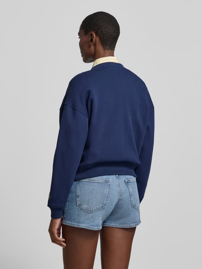 Vrouwenmodel draagt sweatjack met labelprint en knoopsluiting van Polo Ralph Lauren van katoenmix, relaxed fit, ronde hals, labelprintdetails. Ganzekijk achteraanzicht.