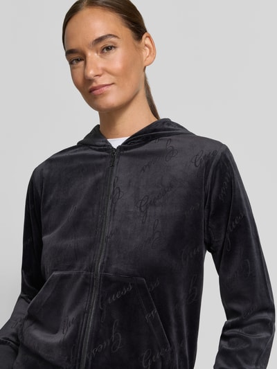Frauenmodel trägt Sweatjacke mit Logo-Muster Modell 'LOREN' von GUESS in Anthrazit, samtige Textur, Nahaufnahme Oberkörper.