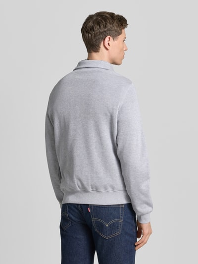 Męski model nosi Regular Fit Sweatshirt aus reiner Baumwolle od Lacoste, szara melanżowa bawełna, długi rękaw, kołnierzyk polo, logo, ripp, krój regular fit, zdjęcie całej sylwetki z tyłu.
