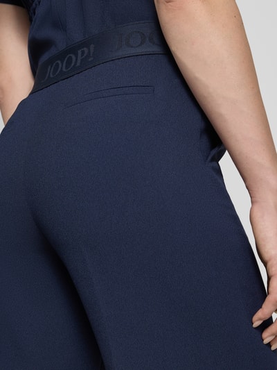 Frauenmodel trägt dunkelblaue Straight Fit Stoffhose mit Logo-Detail von JOOP!, elastischer Bund, feine Textur, Nahaufnahme Hüfte. Modell 'Paulien', Damen Stoffhose, Ziernaht, Bundweite 33 cm, Innenbeinlänge 81 cm.