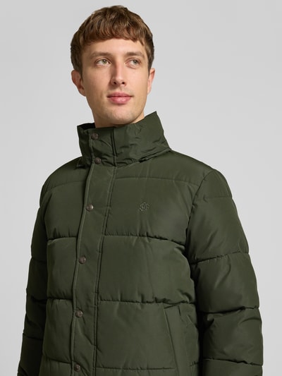 Männermodel trägt Steppjacke mit Kapuze und Reißverschluss von Superdry in Dunkelgrün, sichtbare Knopfleiste, Nahaufnahme Oberkörper. Regular Fit, Stehkragen, verdeckter Reißverschluss, Rückenlänge 71 cm, Schulterbreite 50 cm, Brustweite 56 cm, Ärmellänge 83 cm.