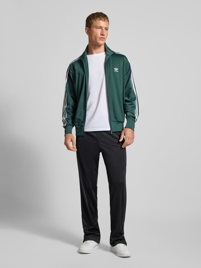 Männermodel draagt Regular Fit Sweatjacke met opstaande kraag model 'Bird' van adidas Originals, groene elastische materiaalmix, gestikt logo, steekzakken met ritssluiting, elastische boorden, ruglengte 72 cm, mouwlengte 66 cm, ganzkörperansicht van voren.