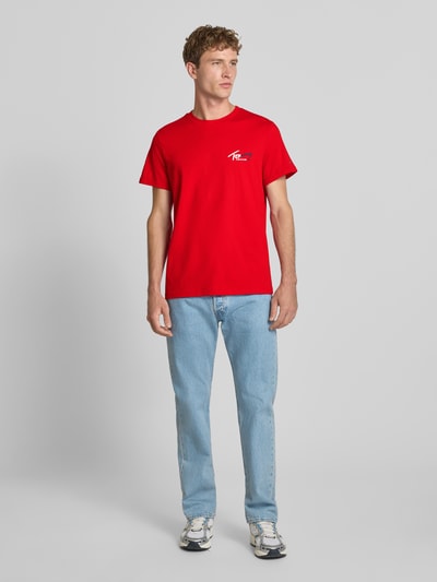 Männermodel trägt Slim Fit T-Shirt aus reiner Baumwolle von Tommy Jeans in leuchtendem Rot, glatte Textur, Ganzkörperansicht von vorne.