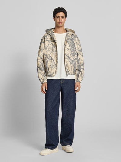 Männermodel trägt Jacke mit Kapuze und Logo von KARL KANI, Reine Baumwolle, Regular-Fit, Allover-Look, Reißverschluss, Ganzkörperansicht von vorne.