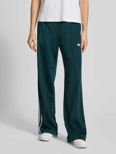Frauenmodel trägt Sweatpants mit elastischem Bund von adidas Originals in dunklem Grün, Lockerer-Schnitt, Label-Stitching, Reißverschlusstaschen, Innenbeinlänge bei Größe S: 80 cm, Ganzkörperansicht von vorne.