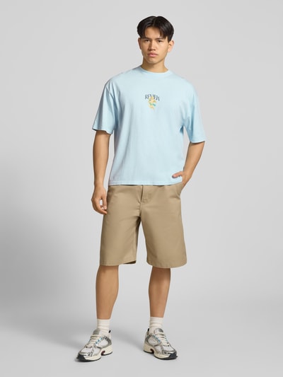 Männermodel trägt T-Shirt mit überschnittenen Schultern von REVIEW aus Reine Baumwolle mit Label-Print, Lockerer-Schnitt, Rundhalsausschnitt, Herren T-Shirt, Rückenlänge 70 cm bei Größe M, Ganzkörperansicht von vorne.