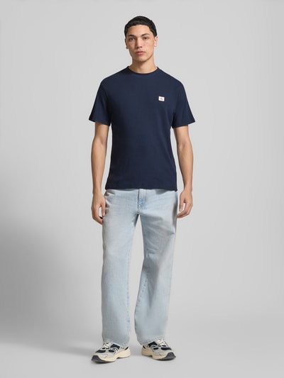 Männermodel trägt Regular Fit T-Shirt mit Logo-Patch von Calvin Klein Jeans in Dunkelblau, Baumwoll-Mix, Strukturmuster, Rundhalsausschnitt, Herren T-Shirt, Rückenlänge 68 cm bei Größe M, Ganzkörperansicht von vorne.