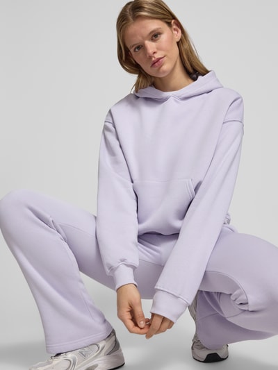 Modelka kobieca nosi Hoodie z kieszenią typu kangur model 'Iconic' od Gina Tricot, bawełniany miks, krój relaxed fit, kolor jasnofioletowy, widok całej sylwetki z przodu.