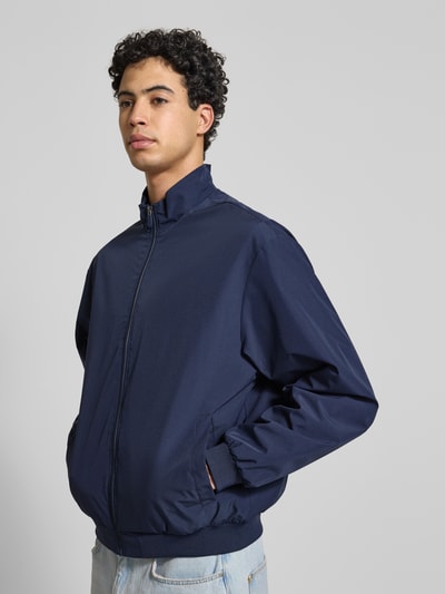 Männermodel trägt Regular Fit Jacke mit Stehkragen Modell 'Charge' von JACK & JONES in Dunkelblau mit Reißverschluss, Eingrifftaschen, elastische Abschlüsse, Rückenlänge 66 cm, Schulterbreite 49 cm, Brustweite 50 cm, Ärmellänge 64 cm, Ganzkörperansicht von vorne.