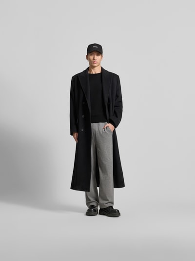 Männermodel trägt Wollpullover aus reiner Wolle von Dsquared2 in Schwarz, körpernahe Passform, Strick-Optik, Rundhalsausschnitt, gerippte Abschlüsse, kombiniert mit langem Mantel und grauer Hose, Ganzkörperansicht von vorne.