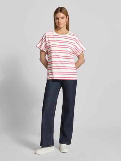 Kobieta modelka nosi damski t-shirt z mieszanki materiałów z domieszką modalu, krój relaxed fit, okrągły dekolt, model 'BARNI' od Soyaconcept, biały w różowe i czerwone paski, gładka faktura, widok całej sylwetki z przodu.