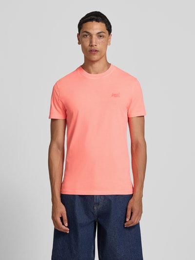 Männermodel trägt T-Shirt mit Rundhalsausschnitt und Label-Stitching von Superdry in Koralle, Reine Baumwolle, Slim-Fit, Ganzkörperansicht von vorne. Rückenlänge bei Größe M: 66 cm.
