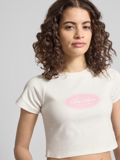 Frauenmodel trägt Cropped T-Shirt mit Logo-Print von ANOTHER COTTON LAB aus reiner Baumwolle in Weiß, Rundhalsausschnitt, Nahaufnahme Oberkörper.