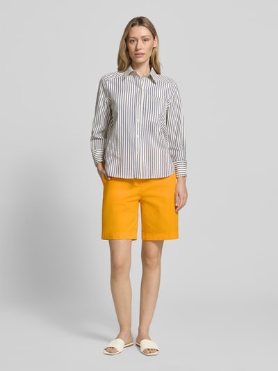 Vrouwenmodel draagt Regular Fit Chino-Shorts uit mix van katoen en lyocell van Tommy Hilfiger, look: effen, met gestikt logo, steekzakken, knoop- en ritssluiting, achterzakken, regular fit pasvorm, kleur geel, stoffen structuur glad, geheelbeeld vooraanzicht.