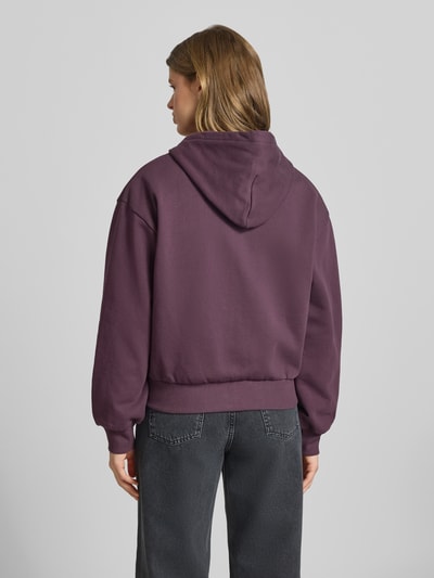 Modelka nosi bluzę rozpinaną z wyhaftowanym logo model 'Casey' od Carhartt Work In Progress, bawełna, krój loose fit, kaptur, zamek błyskawiczny, wpuszczane kieszenie, elastyczne wykończenia, widok całej sylwetki od tyłu.