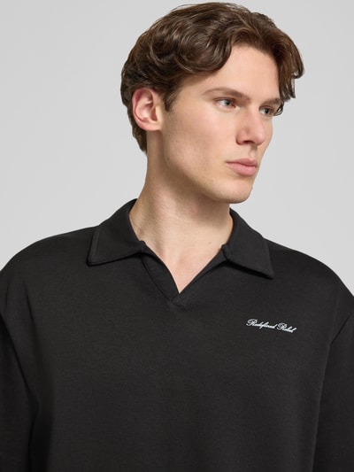 Männermodel trägt Regular Fit Poloshirt mit Logo Modell 'Eddie' von Redefined Rebel aus Baumwoll-Mix in Schwarz, Nahaufnahme Oberkörper. Rückenlänge bei Größe M: 73 cm.