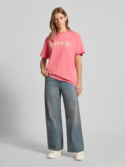 Frauenmodel trägt T-Shirt mit Statement-Print und Rundhalsausschnitt von OH APRIL in Pink, oversized aus reiner Baumwolle, Ganzkörperansicht von vorne.